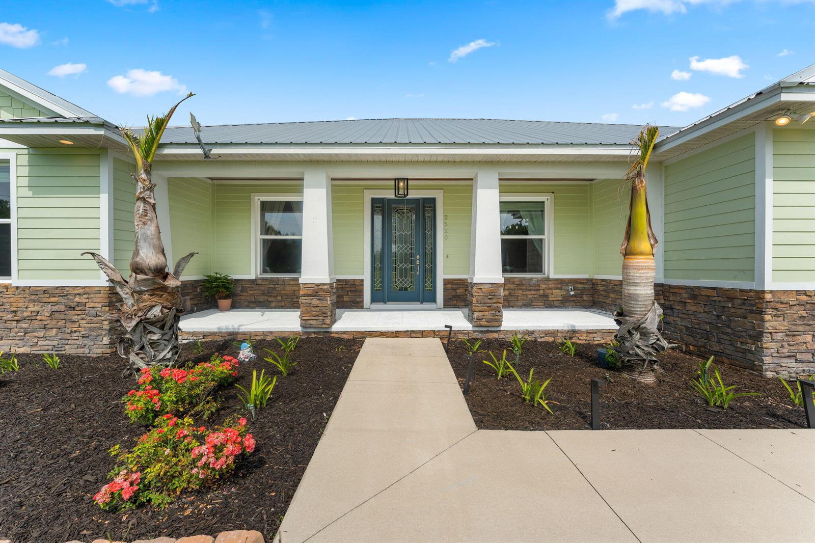 The exterior of a light green house features a stone base, a covered porch, and two palm trees — 2520 Tammy Drive, Mims FL 32754, MIMS, FL