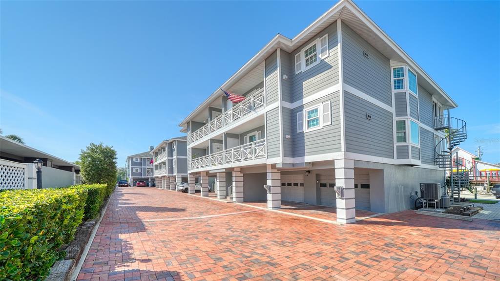 A multi-story gray building with elevated living levels and a brick-paved parking area — 1564 STICKNEY POINT ROAD UNIT 303, SARASOTA, FL
