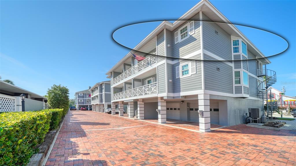 The exterior of a multi-story building with gray siding and a brick-paved driveway — 1564 STICKNEY POINT ROAD UNIT 303, SARASOTA, FL