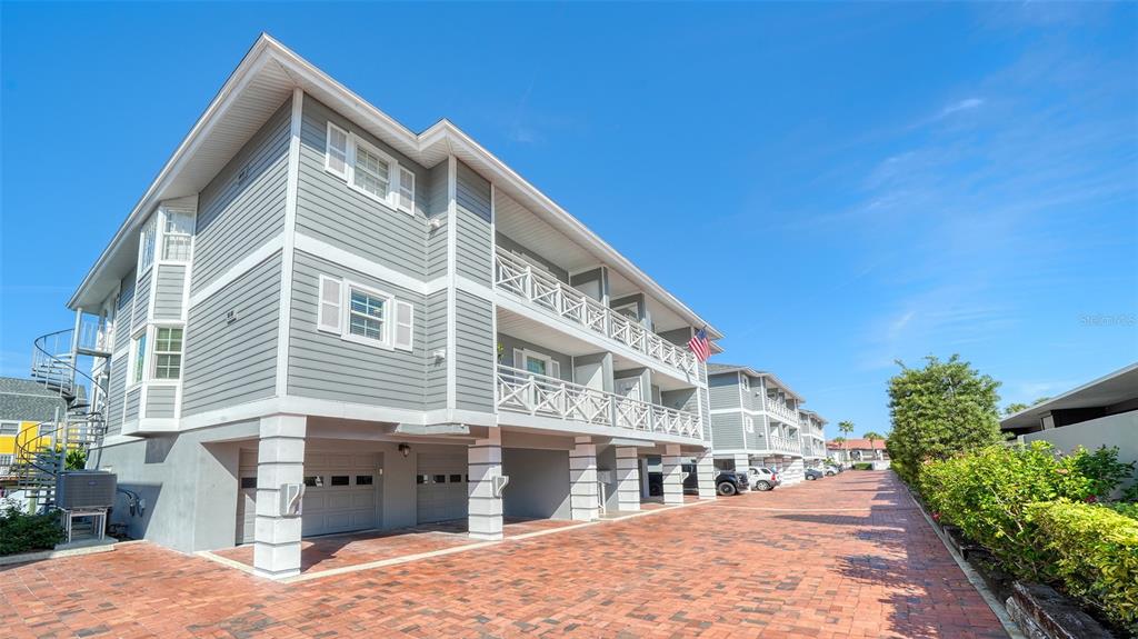 A multi-story building with gray siding, white trim, and a brick-paved driveway — 1564 STICKNEY POINT ROAD UNIT 303, SARASOTA, FL