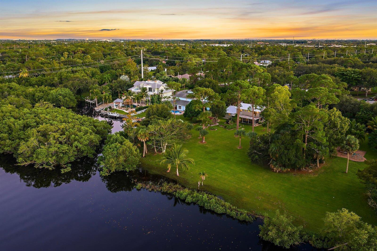 An aerial view shows two houses situated on a large, grassy lot beside a waterway — 6035 N 180th St Street N, Jupiter FL 33458, JUPITER, FL