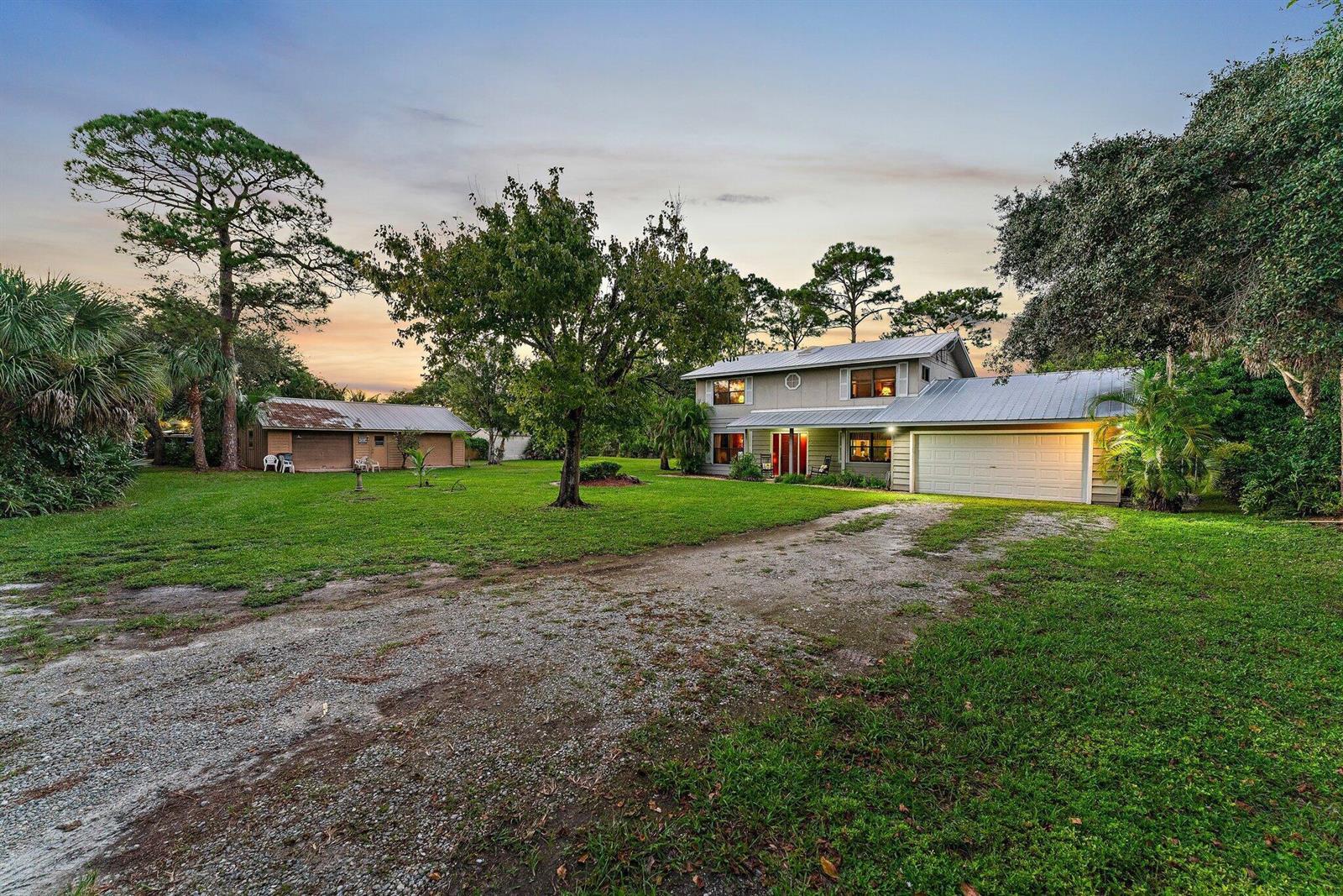 A two-story house with a metal roof and attached garage sits on a grassy lot — 6035 N 180th St Street N, Jupiter FL 33458, JUPITER, FL