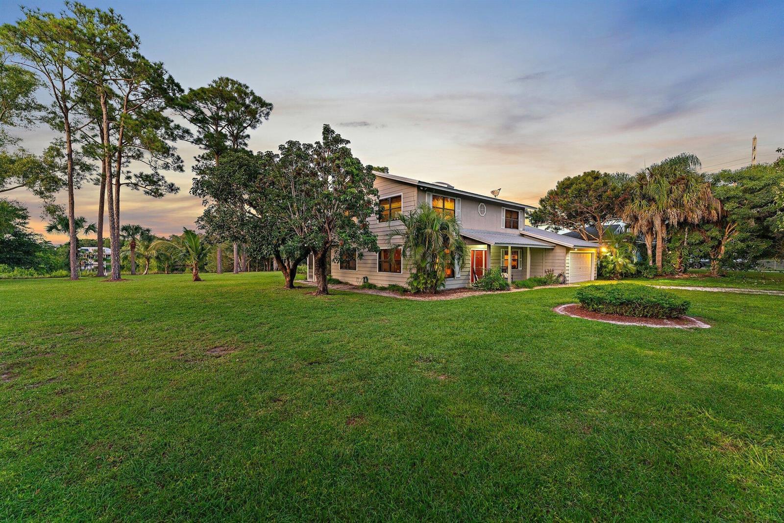A two-story house with light siding sits on a large, grassy lot with mature trees — 6035 N 180th St Street N, Jupiter FL 33458, JUPITER, FL