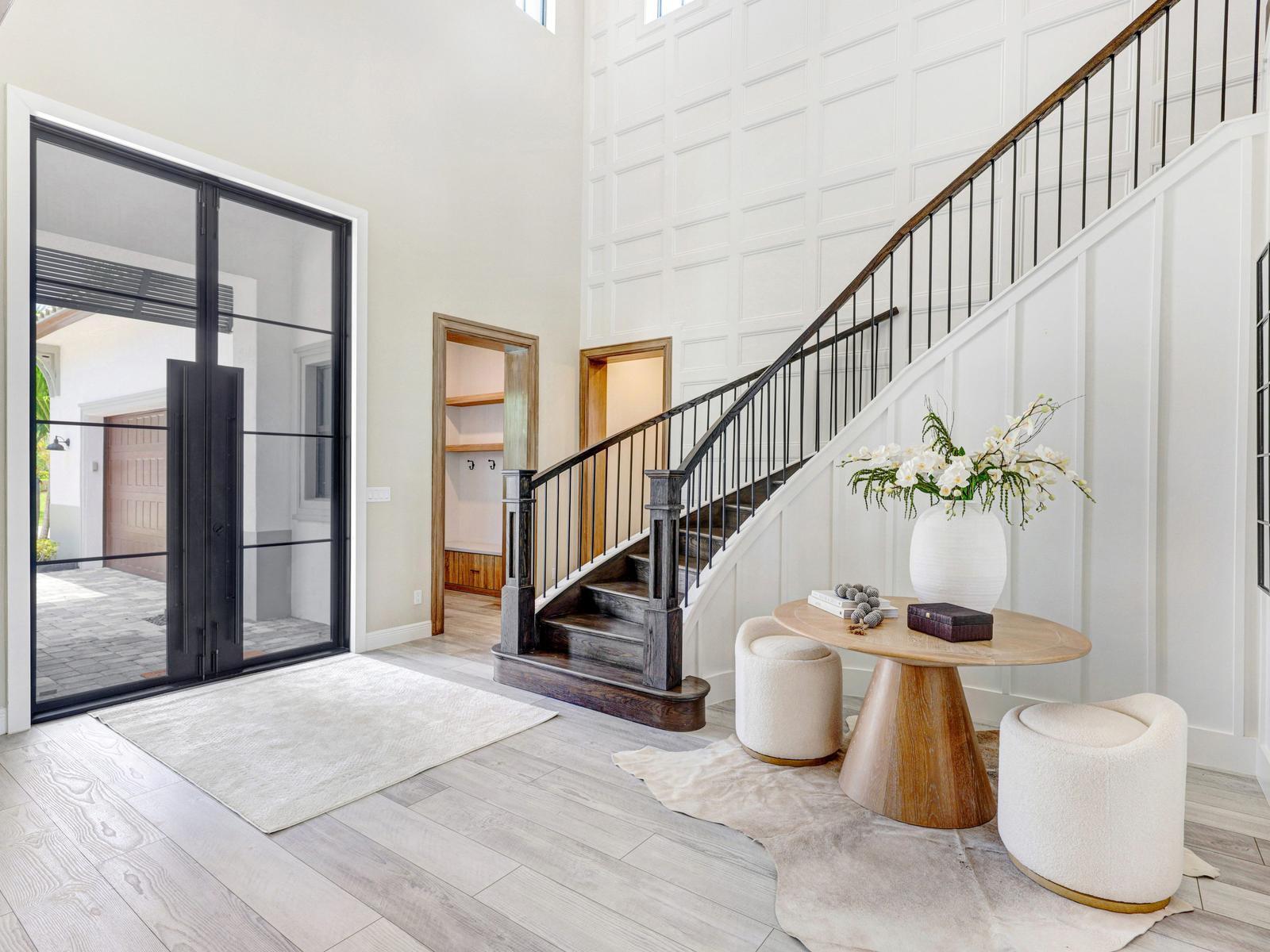 A bright entryway features a grand staircase, a round wooden table, and large glass doors — 8785 Parkland Bay Drive, Parkland FL 33076, PARKLAND, FL