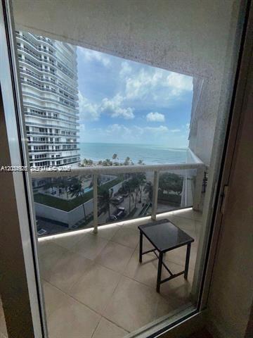 A balcony with a small table overlooks the ocean and a neighboring high-rise building — 9595 Collins Ave # I, Surfside FL 33154, SURFSIDE, FL