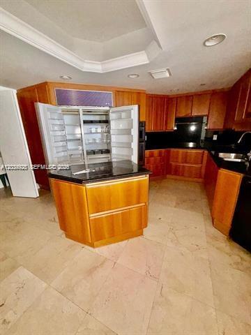 A kitchen features wood cabinetry, black countertops, a central island, and light-colored tile flooring — 9595 Collins Ave # I, Surfside FL 33154, SURFSIDE, FL
