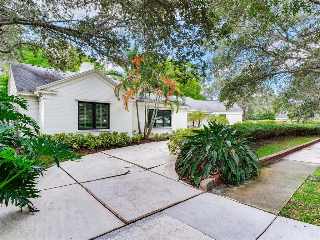 A white brick house with black-framed windows sits behind a concrete driveway and trees — 3401 S ALMERIA AVENUE, TAMPA, FL