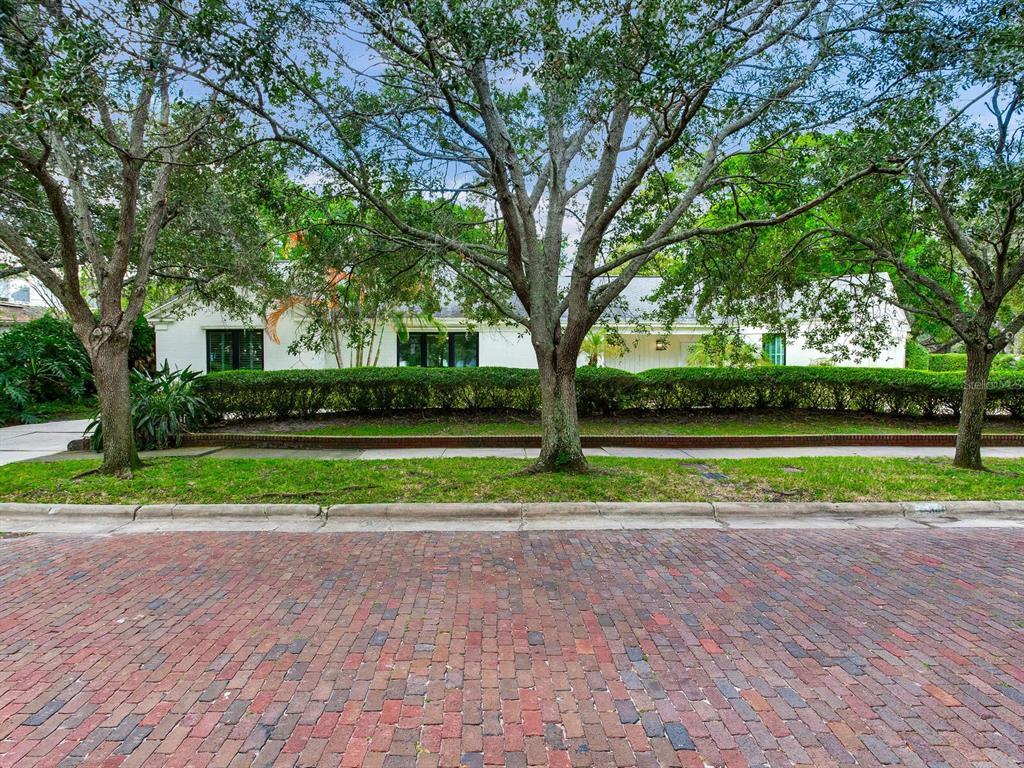 A white single-story house sits behind a manicured hedge and large trees on a brick street — 3401 S ALMERIA AVENUE, TAMPA, FL