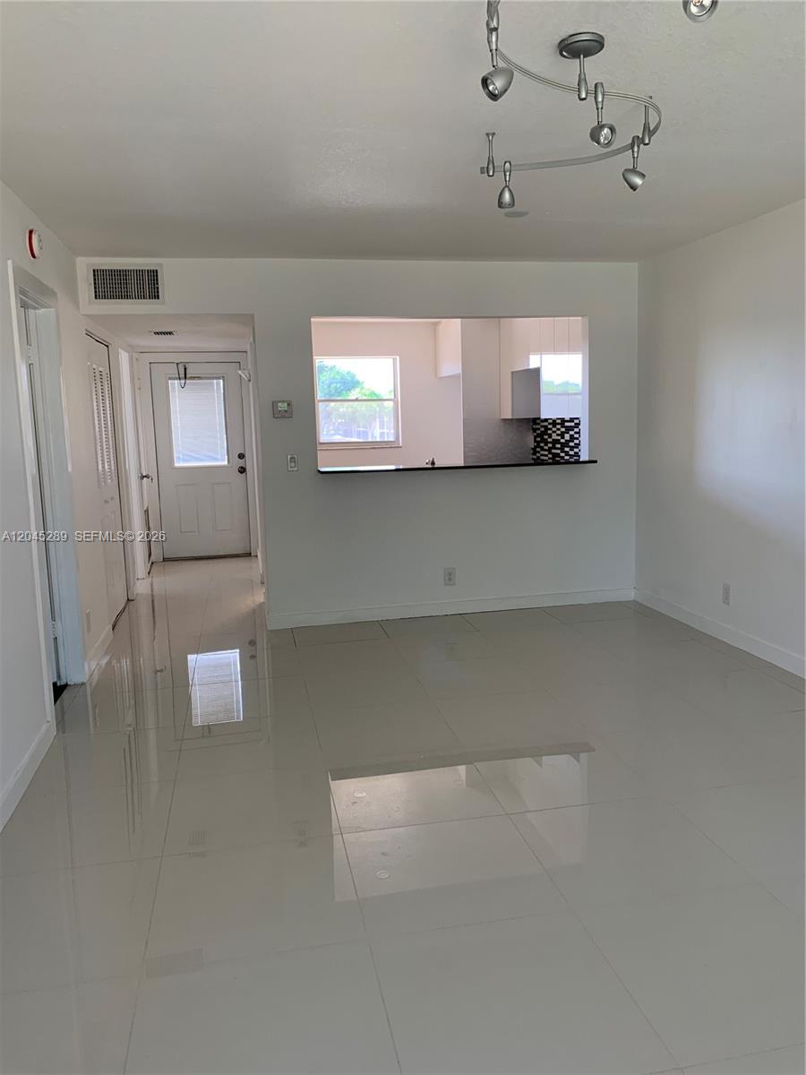 A bright living area features white walls, glossy tile floors, and a kitchen pass-through window — 201 Berkley Rd # 204, Hollywood FL 33024, HOLLYWOOD, FL