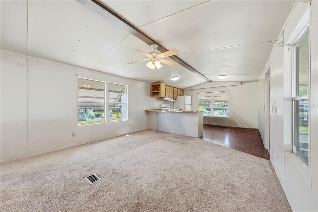 A living room with beige carpet, a ceiling fan, and an open kitchen with cabinets — 30107 GREEN BAY DRIVE, TAVARES, FL