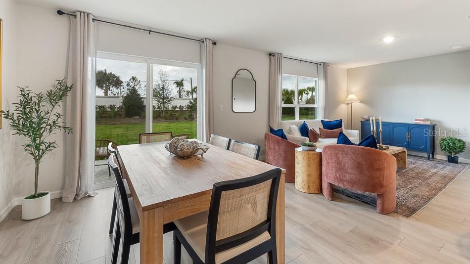 An open-concept living and dining area features light wood flooring, a wooden table, and furniture — 17951 WHEAT STACK COURT, PARRISH, FL