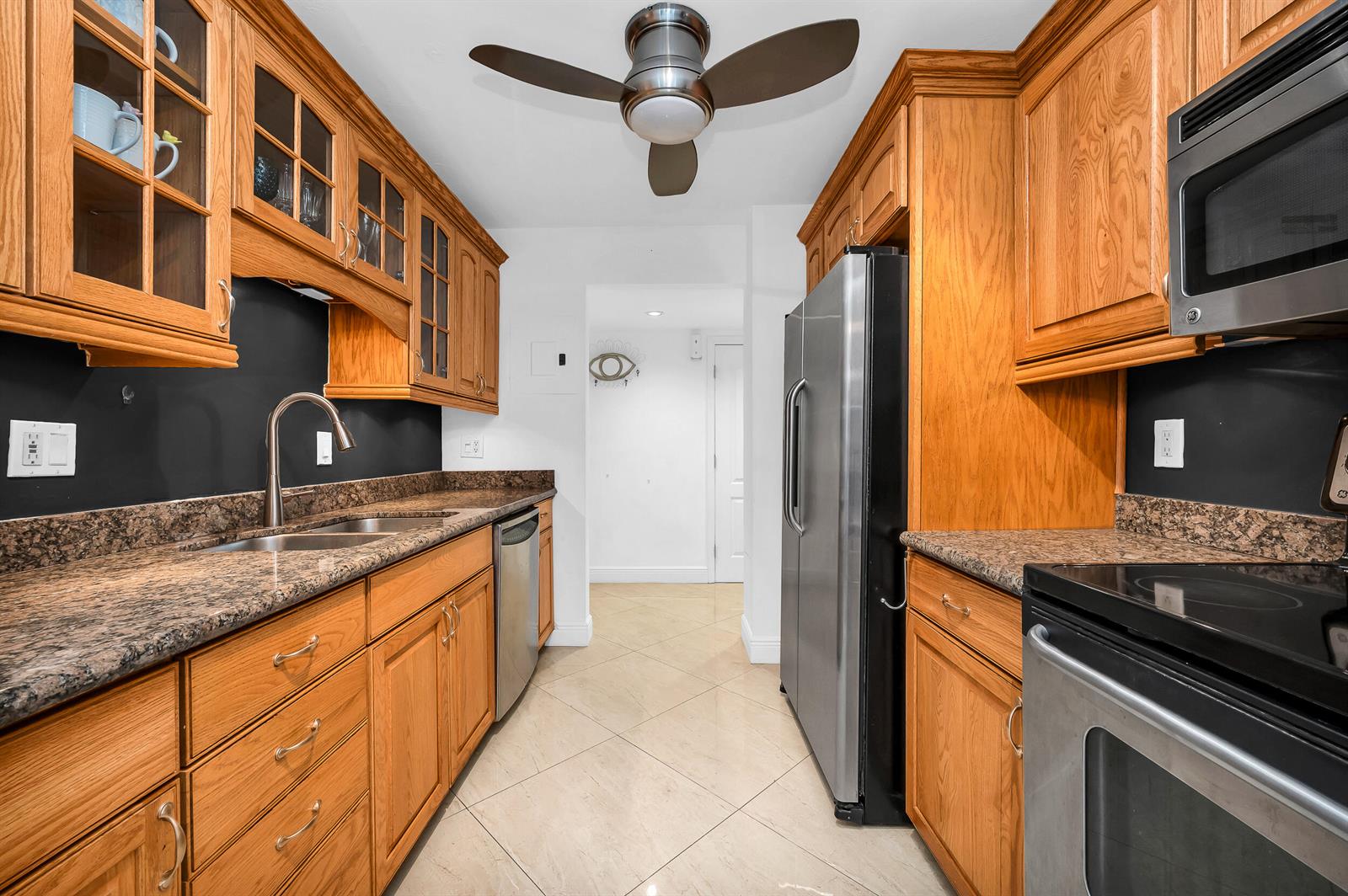 A galley kitchen features oak cabinets, granite countertops, stainless steel appliances, and a ceiling fan — 1111 S Ocean Boulevard # 420, Boca Raton FL 33432, BOCA RATON, FL