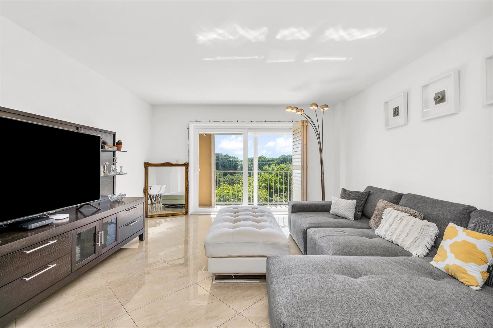 A living room with a grey sectional, white ottoman, tile floors, and a balcony view — 1111 S Ocean Boulevard # 420, Boca Raton FL 33432, BOCA RATON, FL