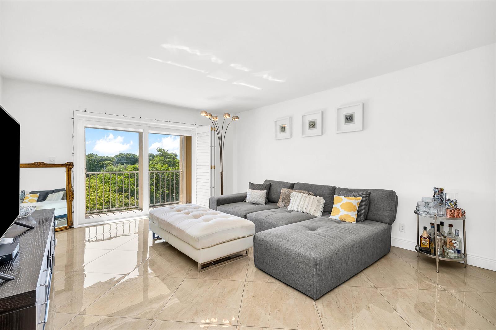 A living room features a grey sectional sofa, white ottoman, and tile flooring near a balcony — 1111 S Ocean Boulevard # 420, Boca Raton FL 33432, BOCA RATON, FL