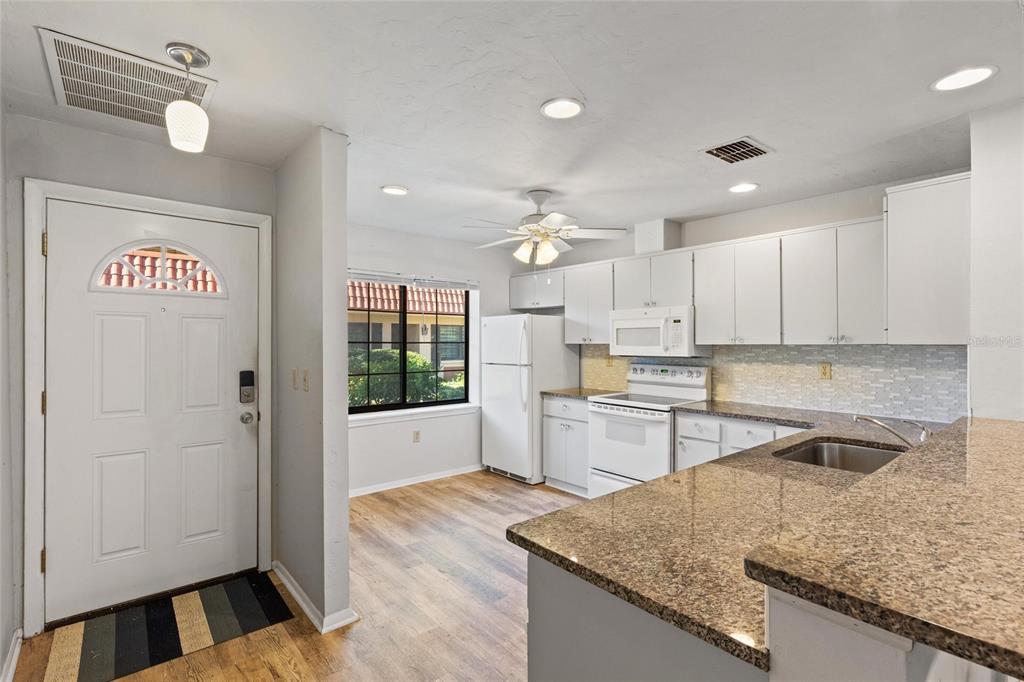 A kitchen with white cabinets, granite countertops, and a dining area near the front door — 19029 US HIGHWAY 19 HIGHWAY N UNIT 24C, CLEARWATER, FL