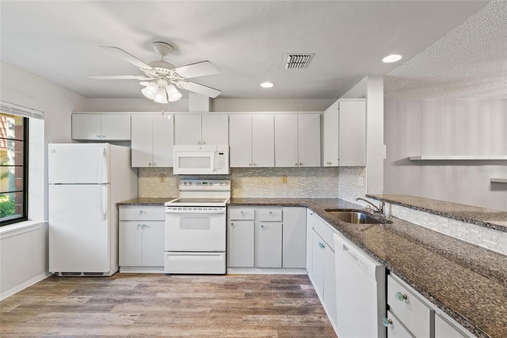A kitchen features white cabinets, granite countertops, white appliances, and wood-look flooring — 19029 US HIGHWAY 19 HIGHWAY N UNIT 24C, CLEARWATER, FL