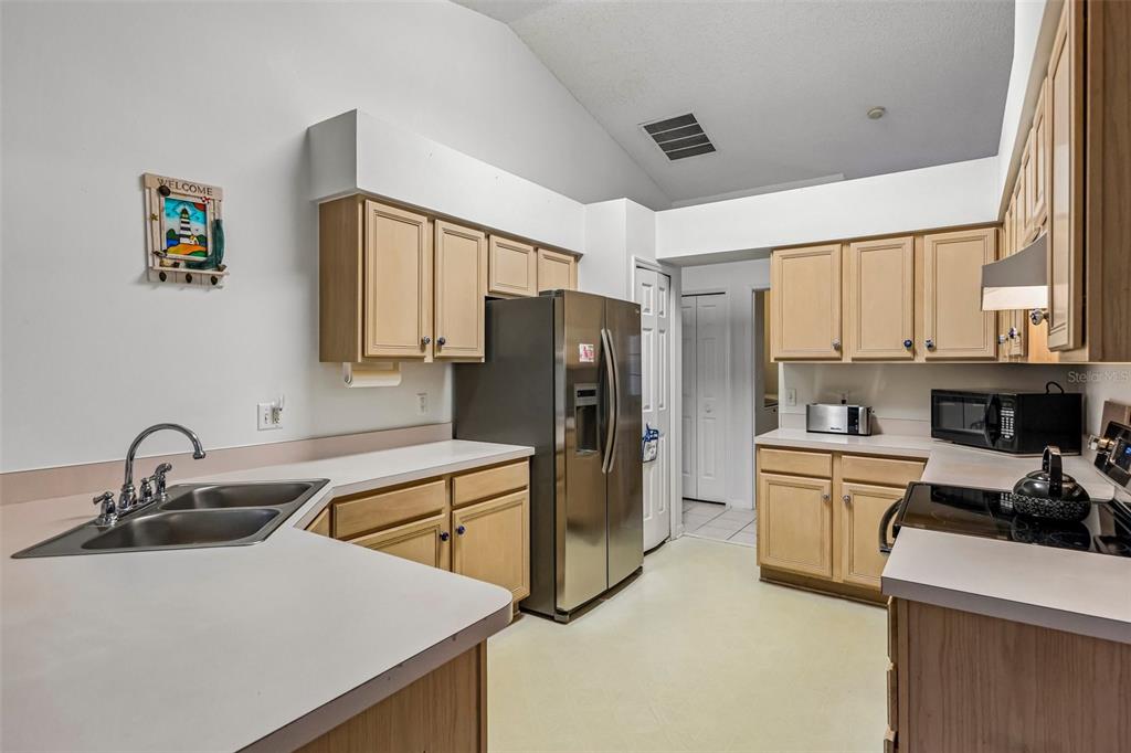A kitchen features light wood cabinets, white countertops, stainless steel appliances, and a double sink — 25111 BONNIE BLUE COURT, LEESBURG, FL
