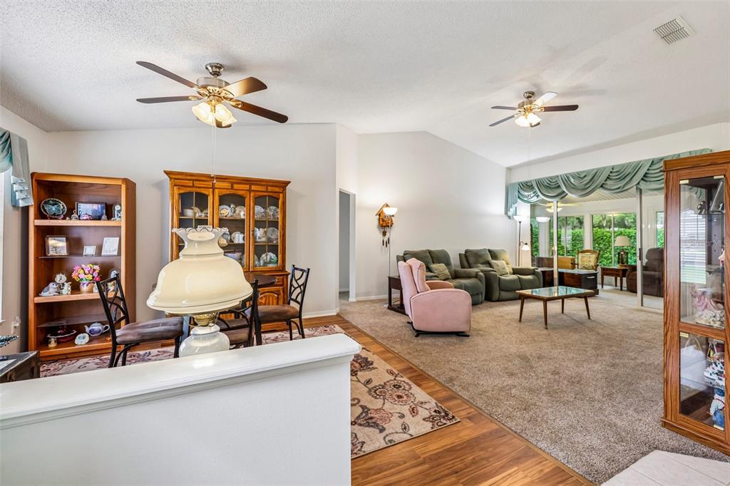 A living and dining area features vaulted ceilings, carpeted and wood flooring, and ceiling fans — 25111 BONNIE BLUE COURT, LEESBURG, FL