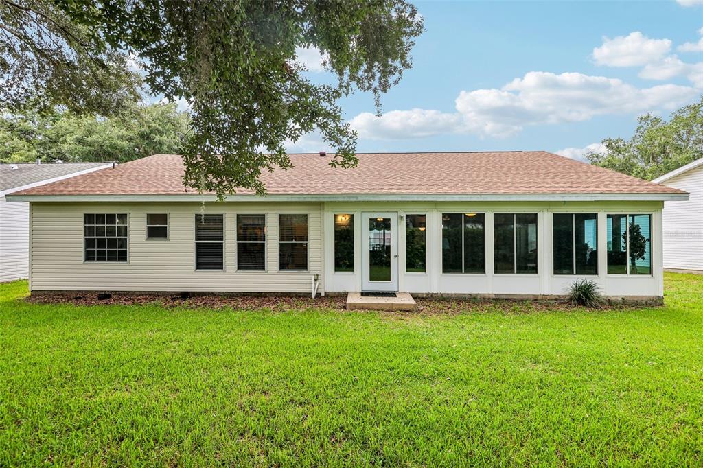 The rear exterior of a single-story house features light-colored siding, a shingled roof, and a sunroom — 25111 BONNIE BLUE COURT, LEESBURG, FL