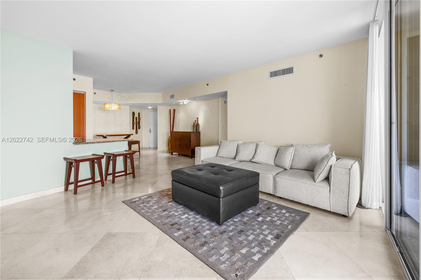 A living room features a light gray sectional sofa, a dark ottoman, and tile flooring — 400 Alton Rd # 907, Miami Beach FL 33139, MIAMI BEACH, FL