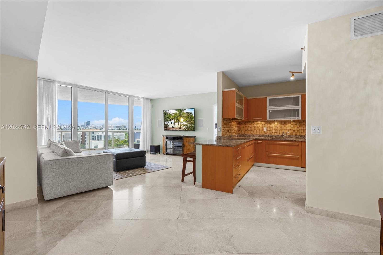 An open-concept living area features a kitchen with wood cabinets and a balcony with views — 400 Alton Rd # 907, Miami Beach FL 33139, MIAMI BEACH, FL