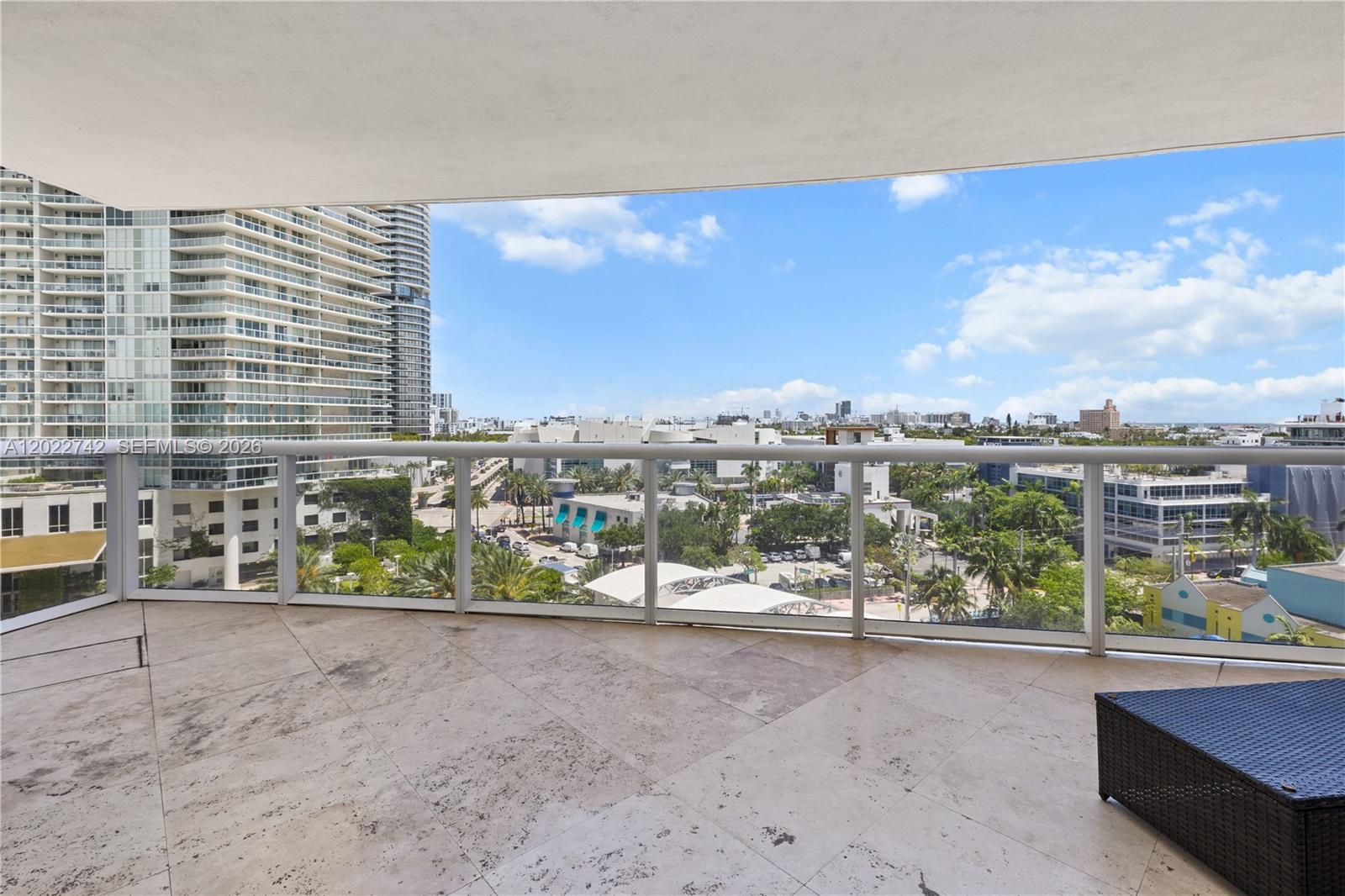 A spacious balcony with stone tile flooring overlooks a city skyline and lush greenery — 400 Alton Rd # 907, Miami Beach FL 33139, MIAMI BEACH, FL