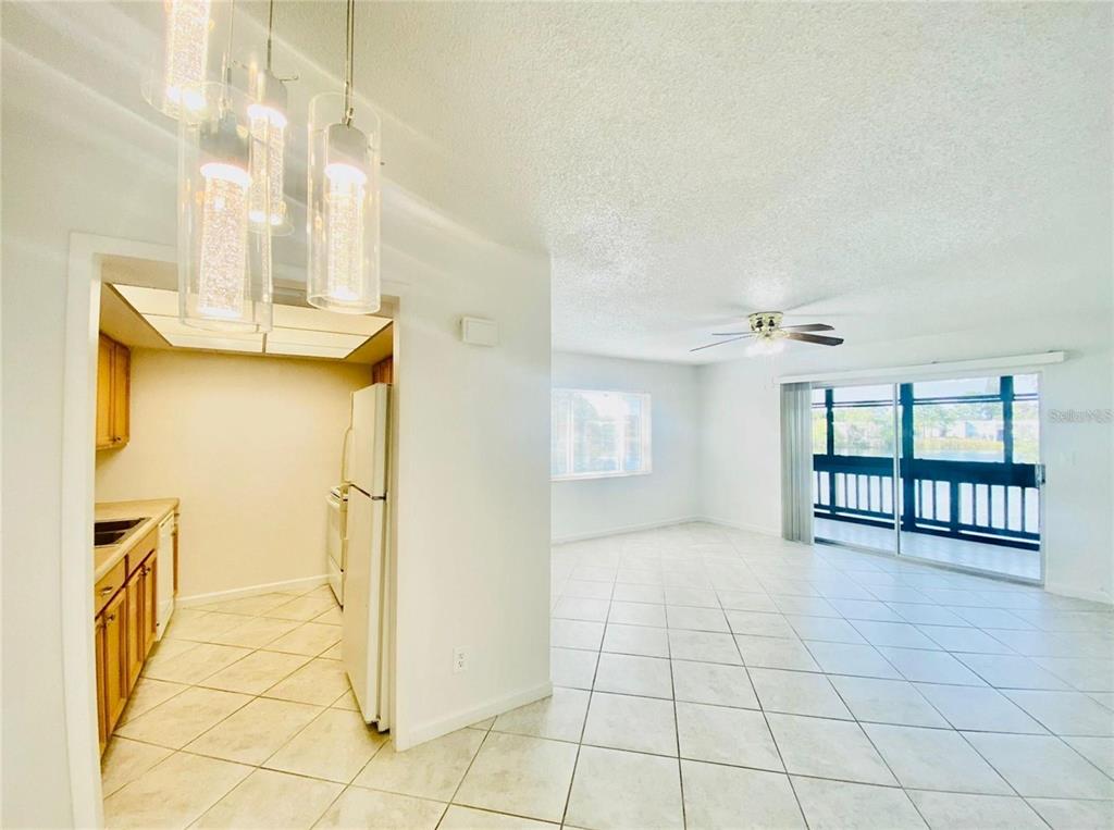 A kitchen with wood cabinets opens into a tiled living area with a sliding glass door — 633 N KEENE ROAD APT C, CLEARWATER, FL