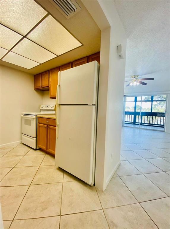 A kitchen with white appliances and wood cabinets opens into a tiled living area — 633 N KEENE ROAD APT C, CLEARWATER, FL