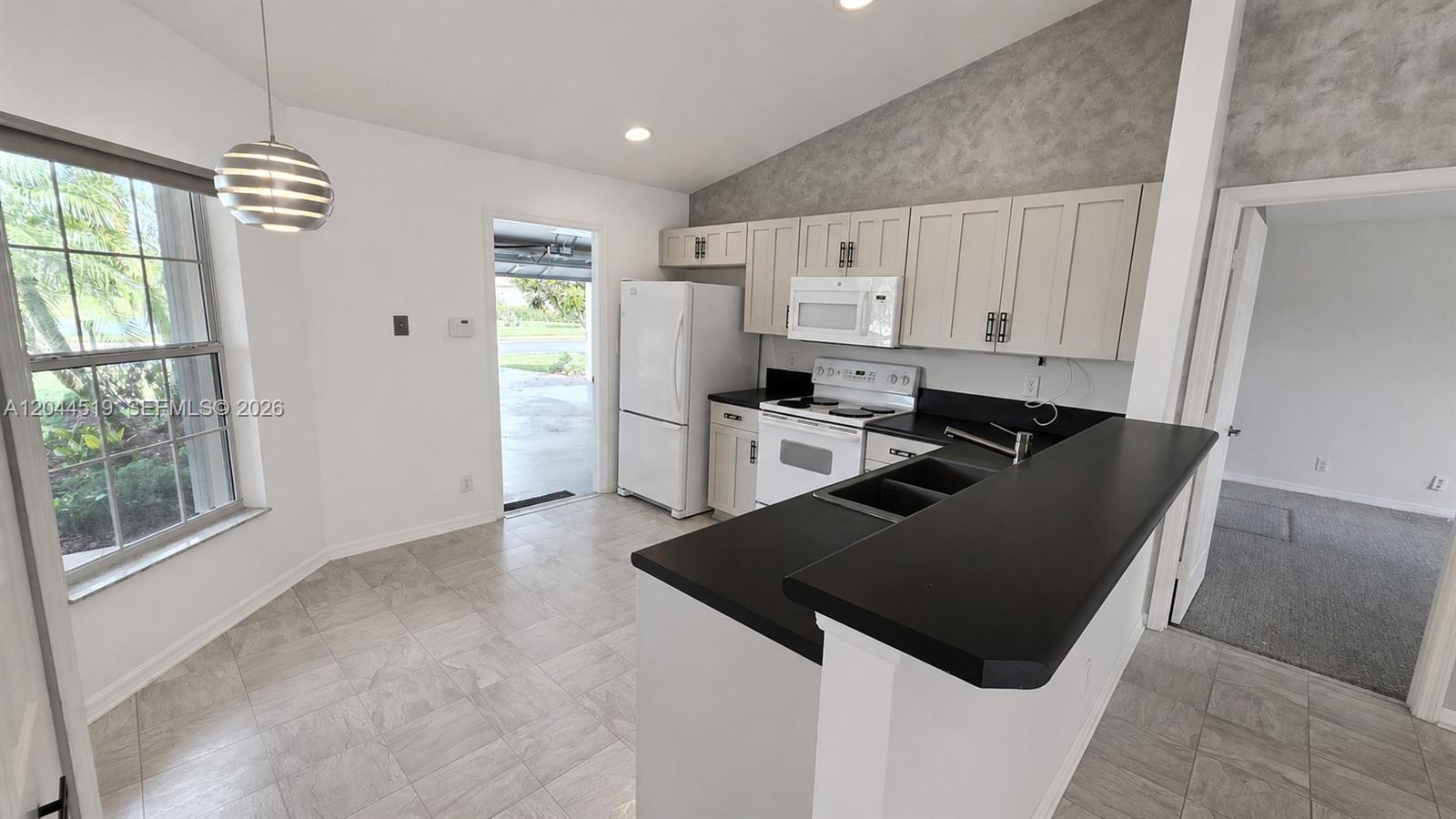 A kitchen features white cabinets, black countertops, a white refrigerator, and light-colored tile flooring — 547 High Hawk Cir # 541, Vero Beach FL 32962, VERO BEACH, FL