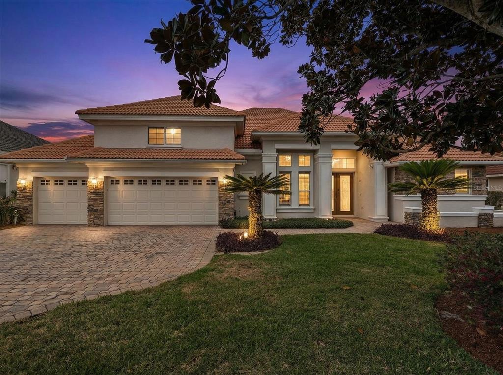 A two-story house with a tile roof, three-car garage, and paved driveway at dusk — 1950 ELKHORN COURT, LONGWOOD, FL