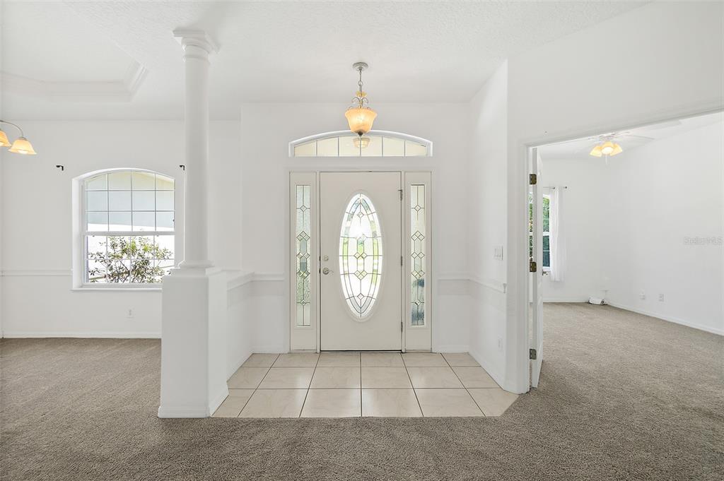 A bright entryway features a white front door with sidelights, tile flooring, and carpeted rooms — 25 FENIMORE LANE, PALM COAST, FL