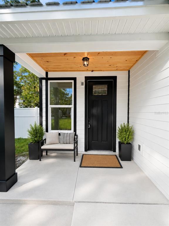 A covered front porch features a black door, a window, a bench, and potted plants — 25 HERNANDEZ AVENUE, PALM COAST, FL