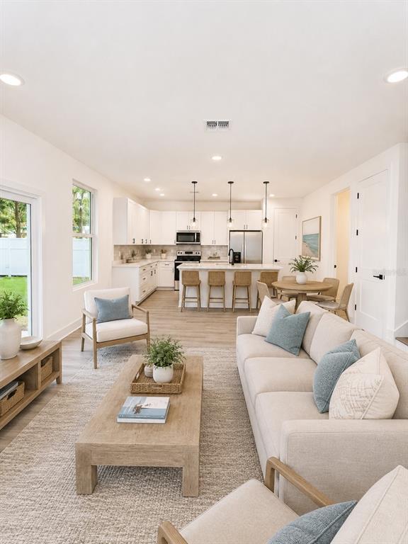 An open-concept living room and kitchen featuring white cabinetry, light wood floors, and neutral furniture — 25 HERNANDEZ AVENUE, PALM COAST, FL