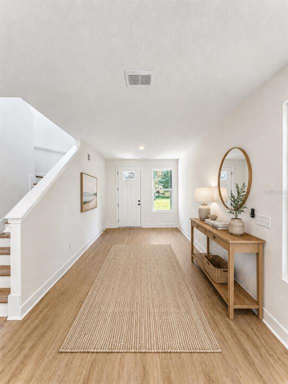 A bright entryway features light wood flooring, a staircase, a console table, and a rug — 25 HERNANDEZ AVENUE, PALM COAST, FL