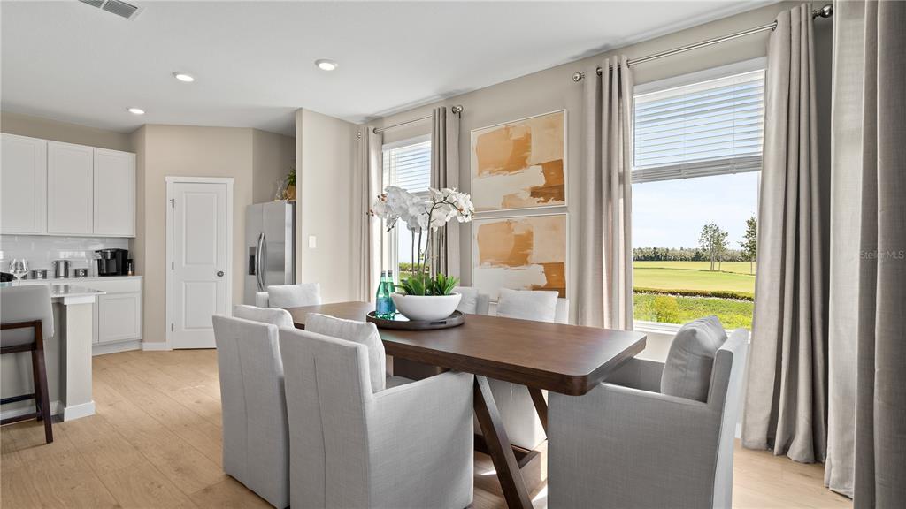 A dining area features a wooden table, upholstered chairs, and large windows overlooking a golf course — 159 GLENFIELD DRIVE, DAVENPORT, FL