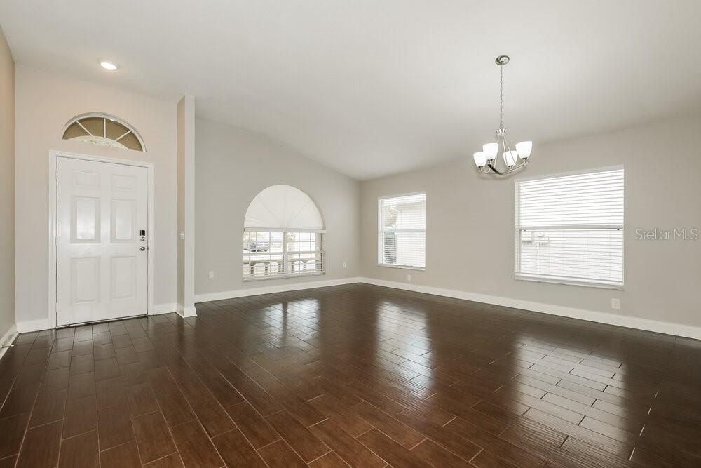 An empty room with dark wood-look tile flooring, light gray walls, and a chandelier — 10124 COLDWATER LOOP, LAND O LAKES, FL
