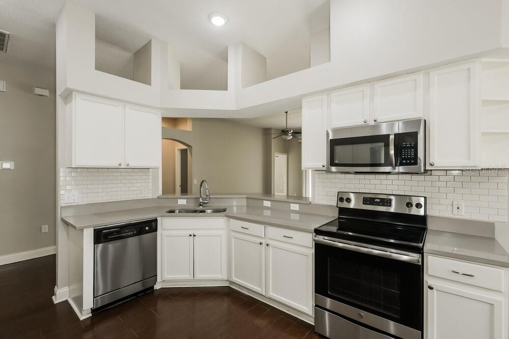 A kitchen with white cabinets, stainless steel appliances, gray countertops, and a white subway tile backsplash — 10124 COLDWATER LOOP, LAND O LAKES, FL
