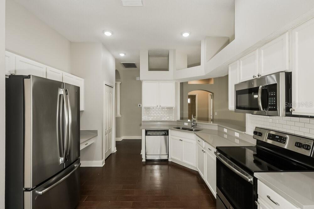 A kitchen with white cabinets, stainless steel appliances, gray countertops, and dark hardwood flooring — 10124 COLDWATER LOOP, LAND O LAKES, FL