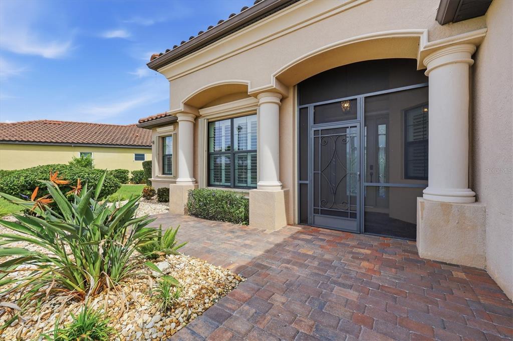 A paved entryway leads to a front door with a screen door and decorative columns — 13652 CLASSICO COURT, VENICE, FL