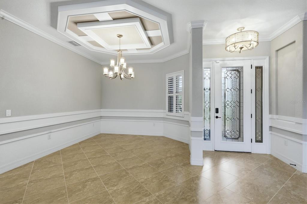 An entryway and dining area feature tile flooring, a tray ceiling, and a decorative front door — 13652 CLASSICO COURT, VENICE, FL
