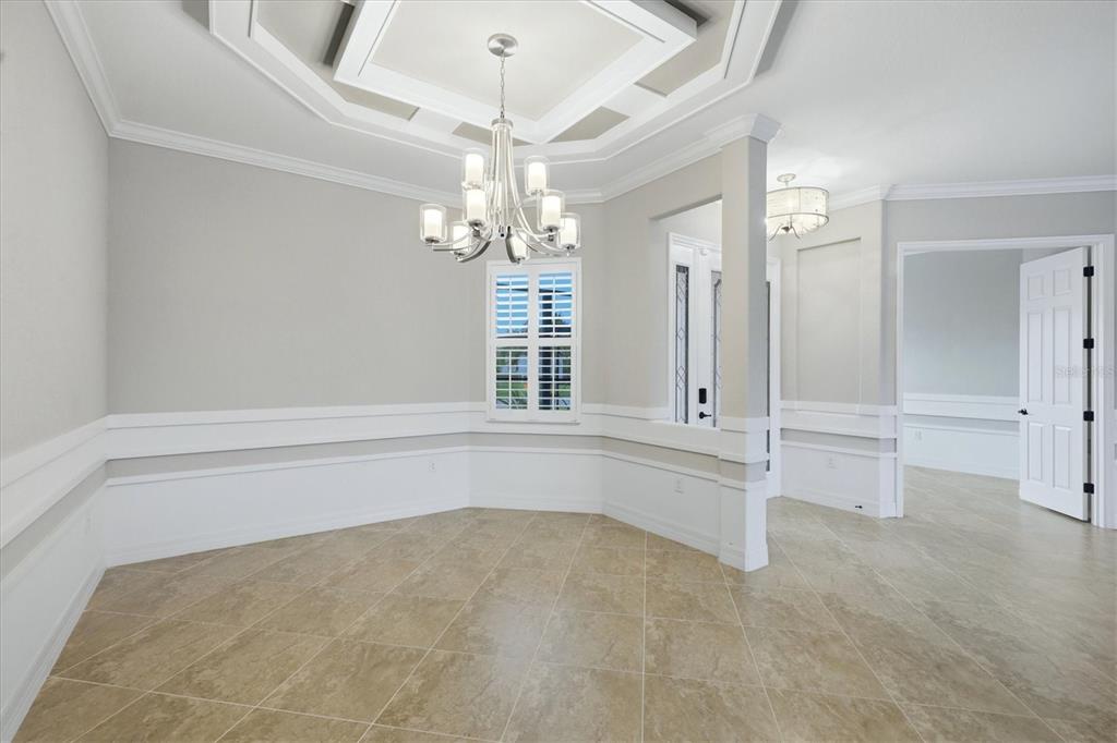 A dining room with tile floors, a tray ceiling, a chandelier, and white wainscoting — 13652 CLASSICO COURT, VENICE, FL