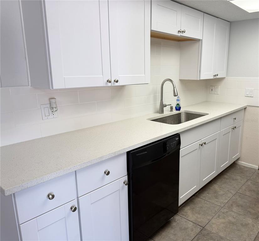 A kitchen features white cabinets, light-colored countertops, a stainless steel sink, and a black dishwasher — 7535 CHRISTINA LANE, PORT RICHEY, FL