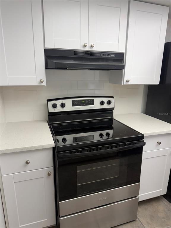 A kitchen features white cabinets, a black electric stove, and a white subway tile backsplash — 7535 CHRISTINA LANE, PORT RICHEY, FL