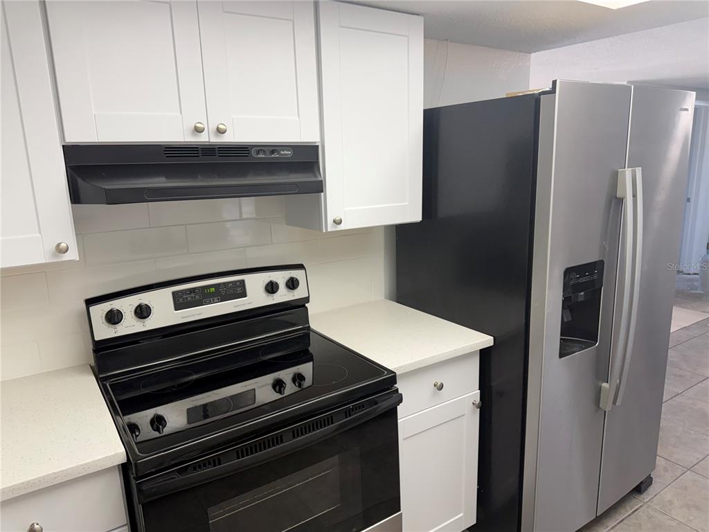 A kitchen features white cabinets, a black electric range, and a stainless steel refrigerator — 7535 CHRISTINA LANE, PORT RICHEY, FL