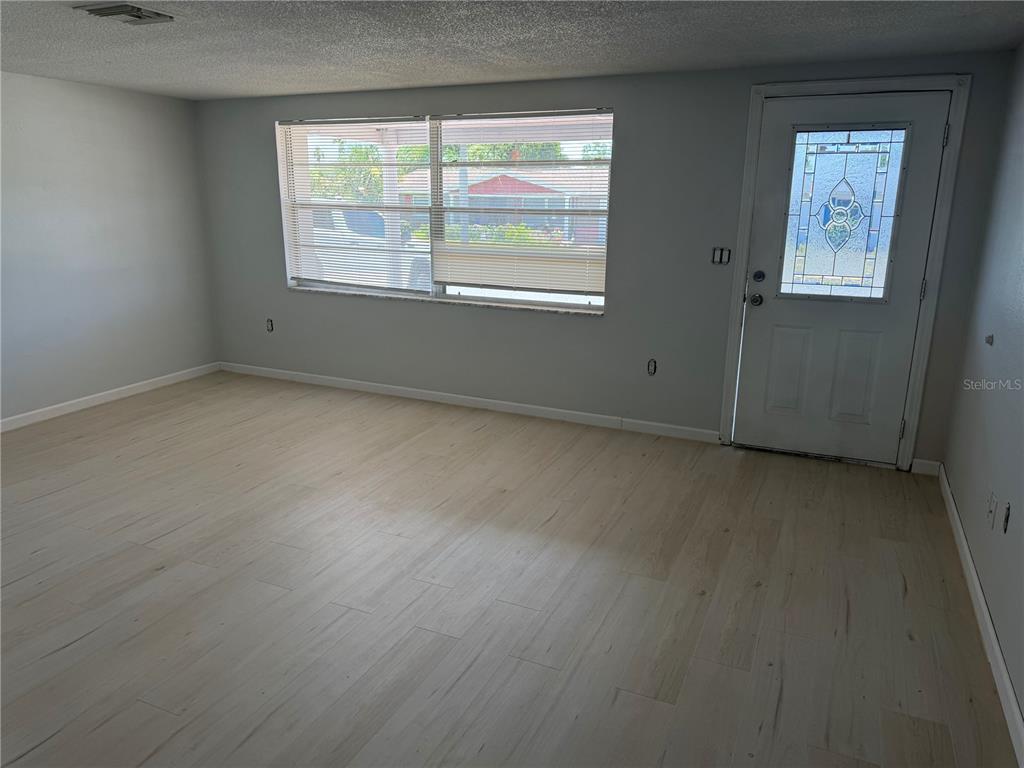 An empty room with light wood-look flooring, gray walls, a large window, and a door — 7535 CHRISTINA LANE, PORT RICHEY, FL