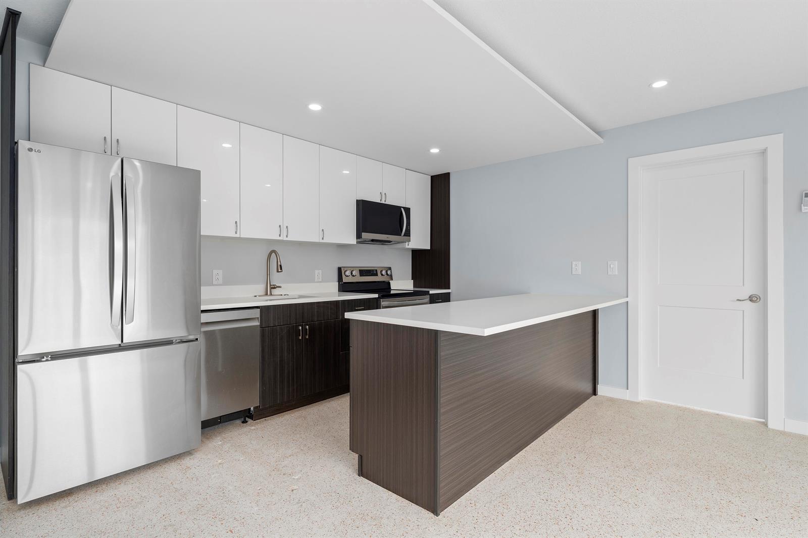 A modern kitchen features white upper cabinets, dark lower cabinets, stainless steel appliances, and an island — 3220 NE 7th Place # 3, Pompano Beach FL 33062, POMPANO BEACH, FL
