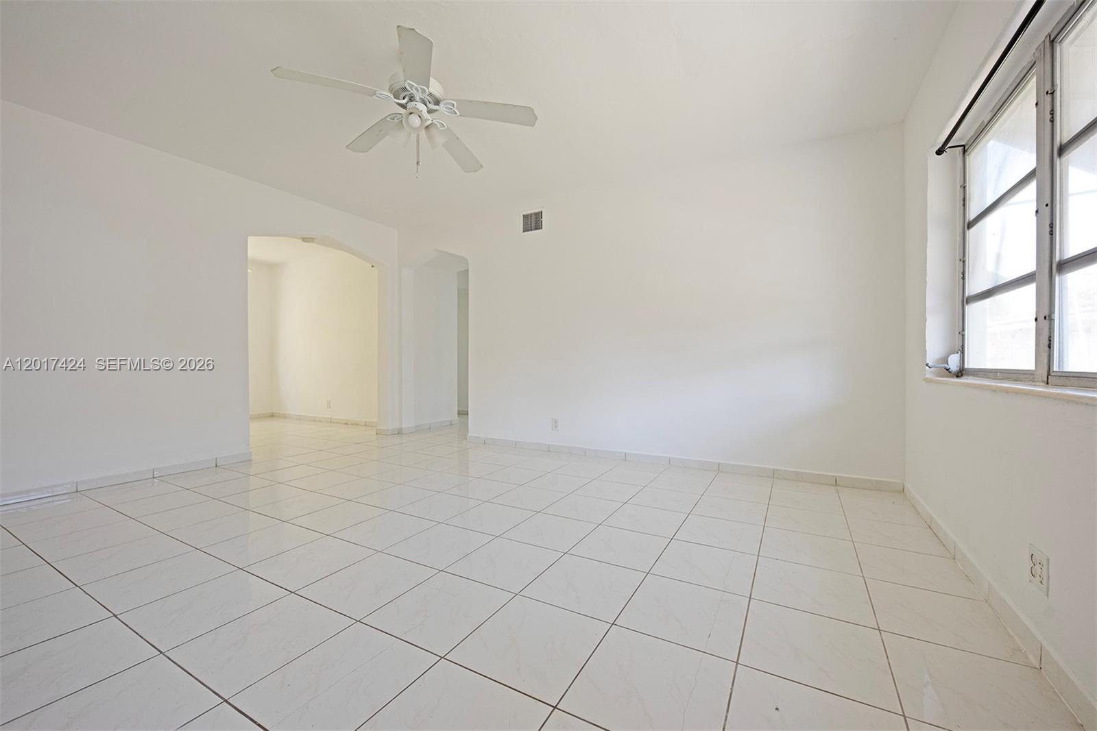 A bright, empty room features white tile flooring, white walls, and a ceiling fan — 1735 Marseille Dr # 2, Miami Beach FL 33141, MIAMI BEACH, FL