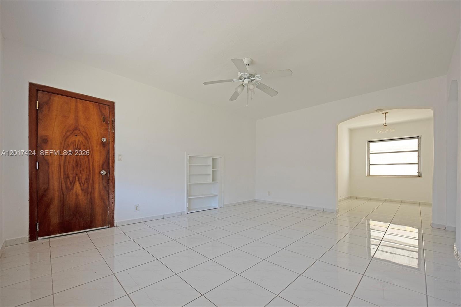 A bright, tiled living room features a wooden front door, built-in shelving, and a ceiling fan — 1735 Marseille Dr # 2, Miami Beach FL 33141, MIAMI BEACH, FL