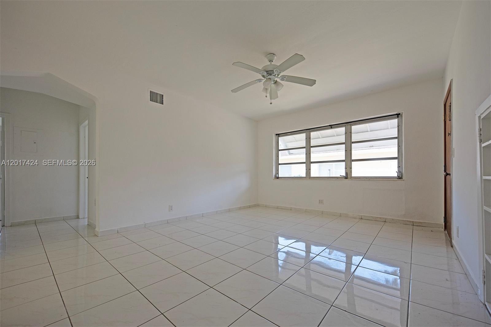 An empty room features white tiled floors, a ceiling fan, and a large window — 1735 Marseille Dr # 2, Miami Beach FL 33141, MIAMI BEACH, FL