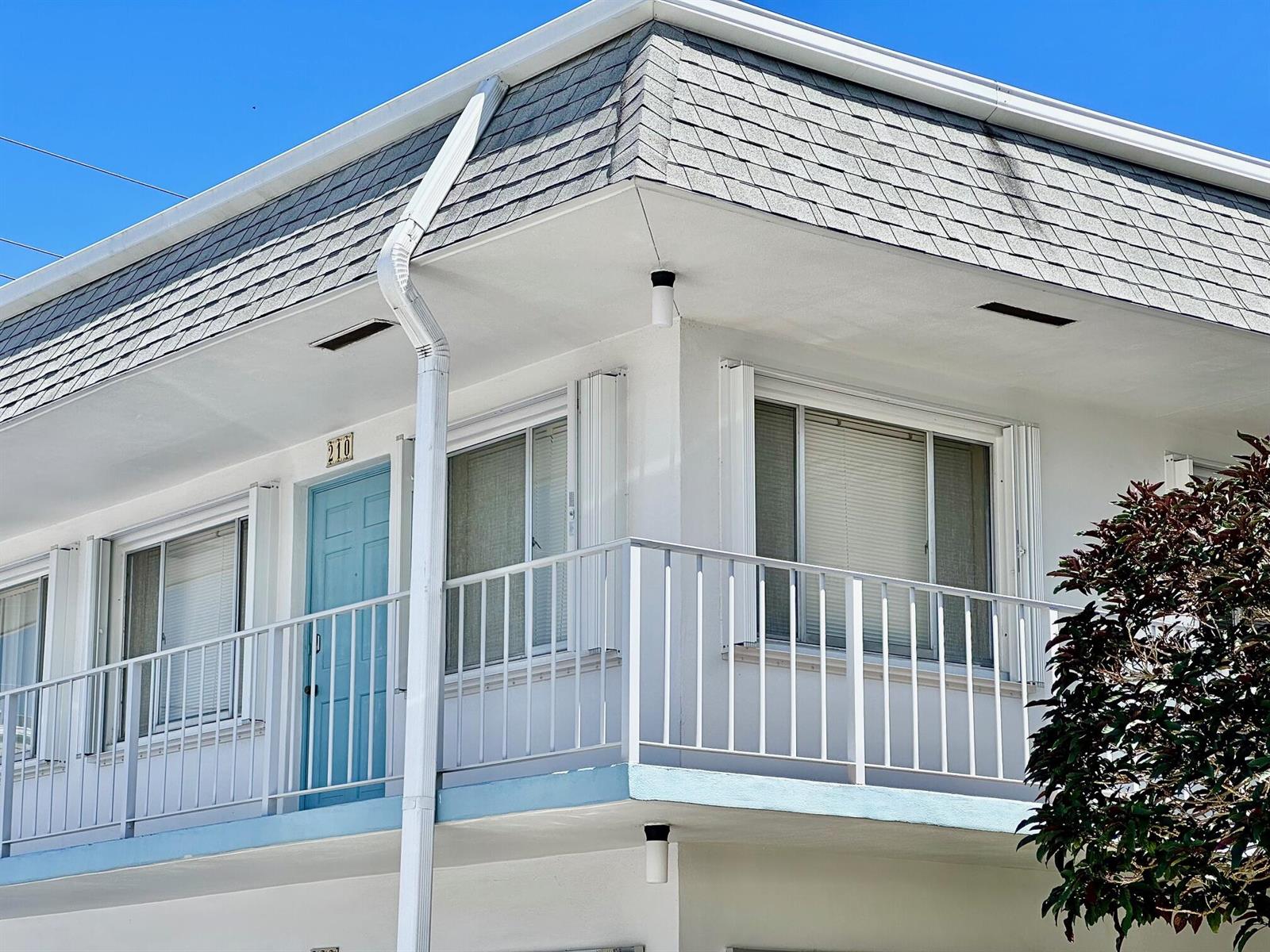 An exterior view of a white building with a blue door, balcony, and gray roof — 2880 Lake Osborne Drive # 210, FL 33461, FL